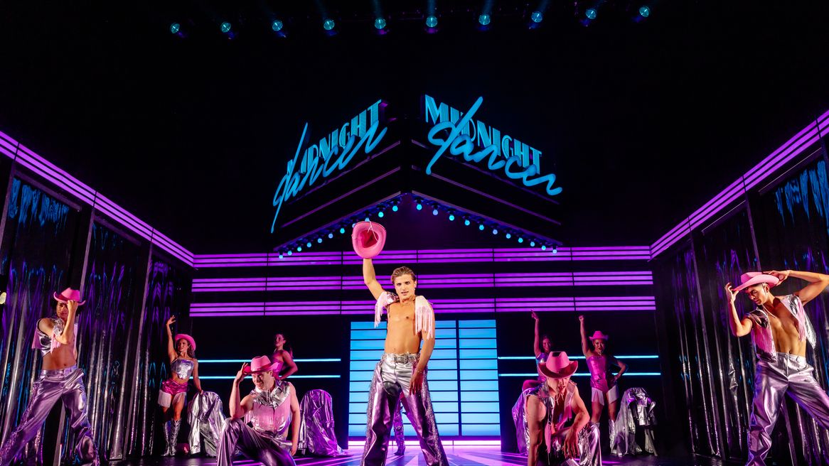 Dancer Nikita dressed as a cowboy dancing arm in the air with a troupe of dancers behind him