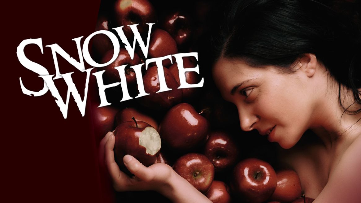 Woman holding a red apple, which has had a bite out of it with more apples in the background. 