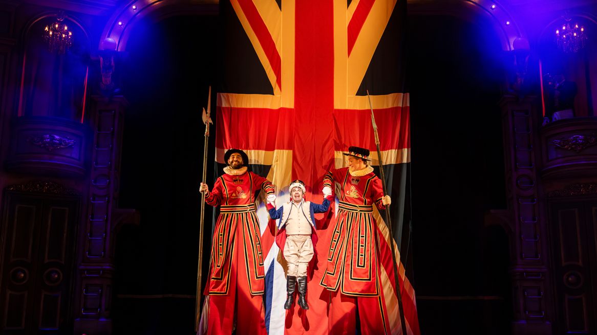 A small man dressed as a king is held up by two beefeaters on stilts