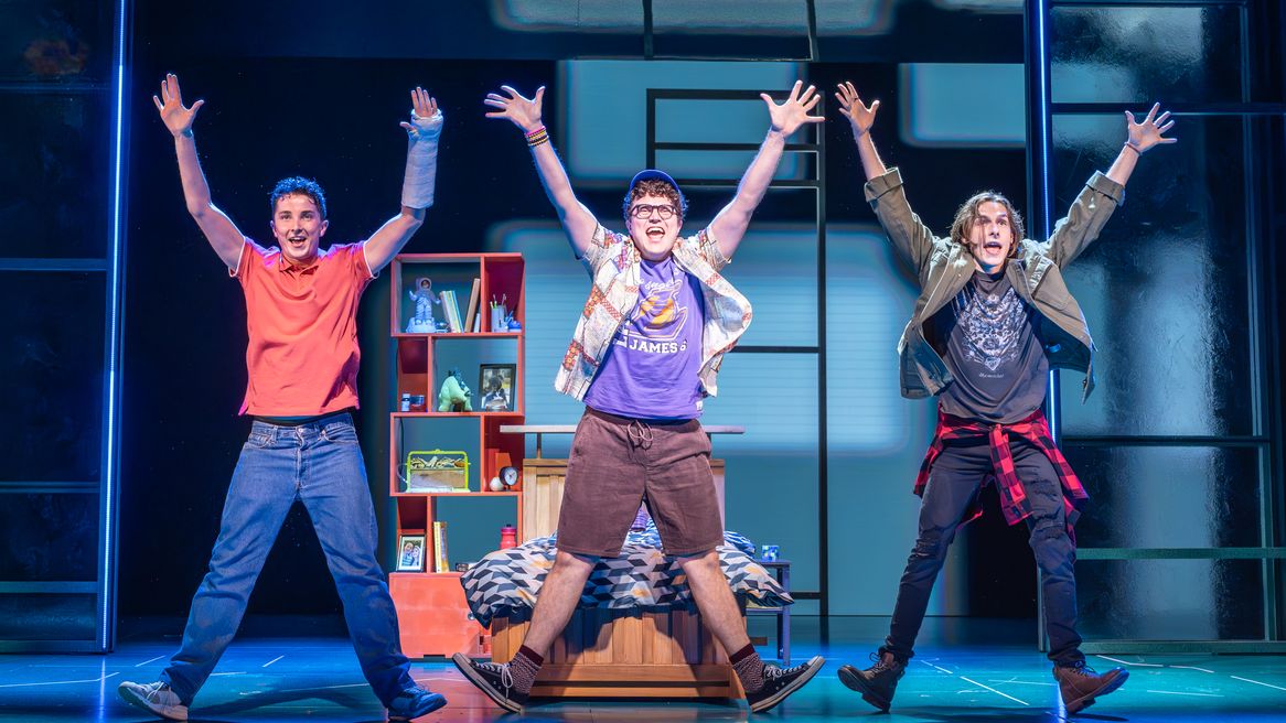 Three teen boys pose in identical star jump positions in a bedroom