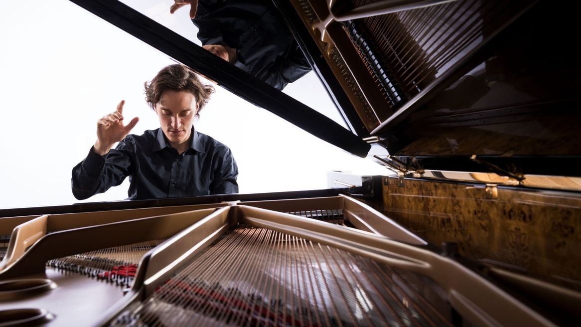 Man sat at a piano with his hand in the air.