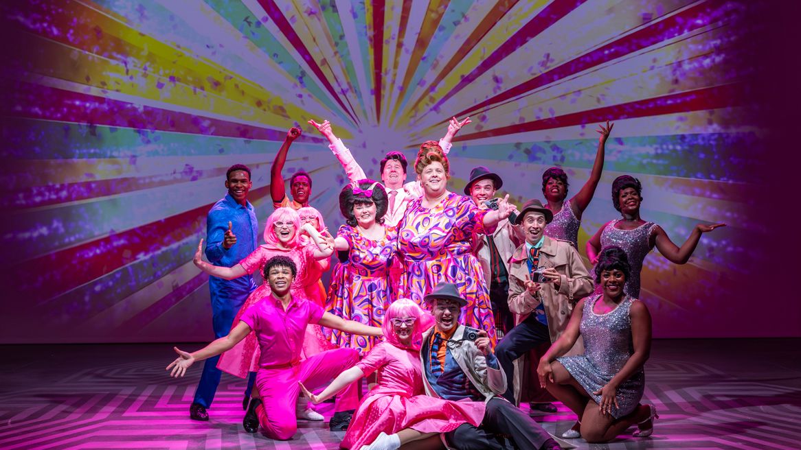 A group of people in brightly coloured sixties themed clothing pose happily