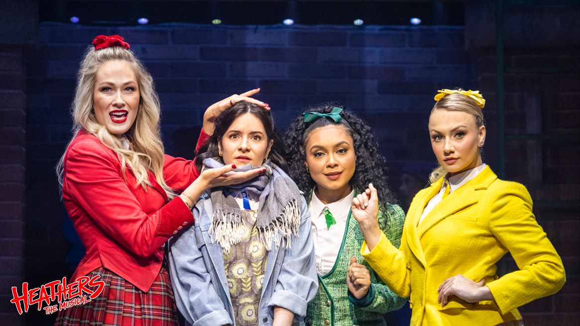 Three girls in matching red, yellow and green outfits frame the face of a girl in ugly clothing.