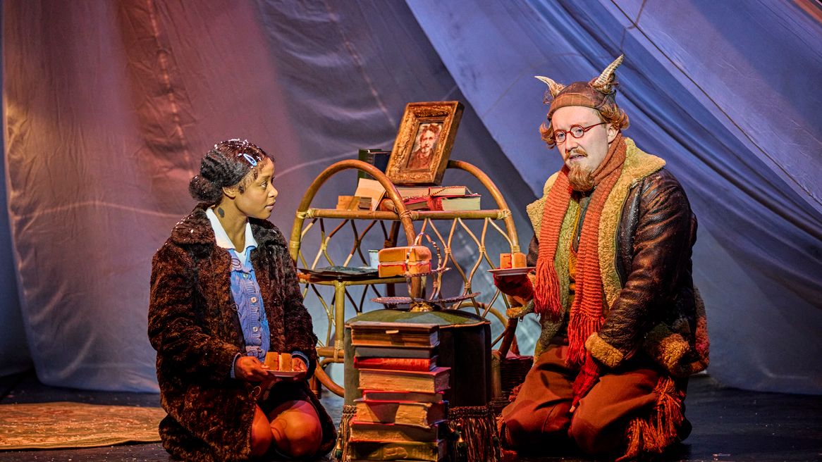 A young girl and a goat man sit down to tea over a stack of books
