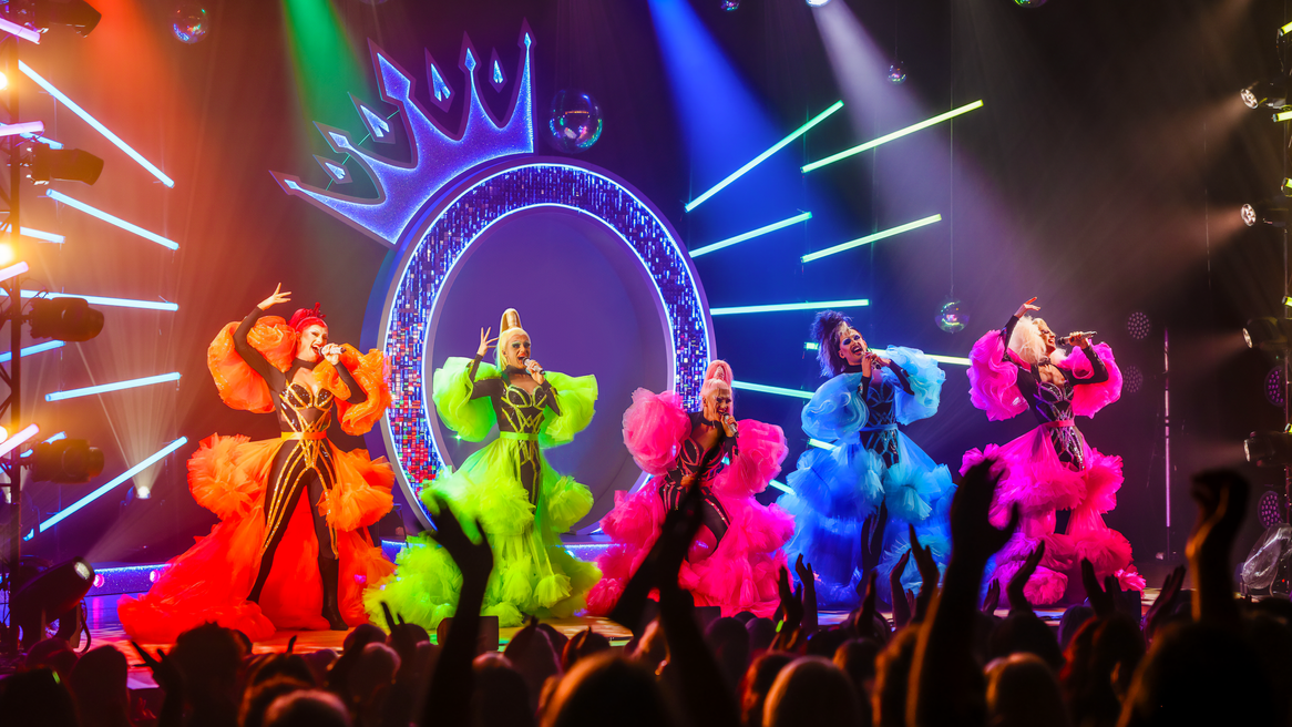 Five drag queens in brightly coloured flamboyant outfits dance