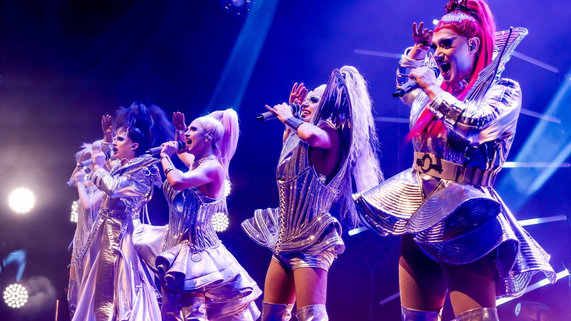 Five drag queens in silver popstar outfits perform together