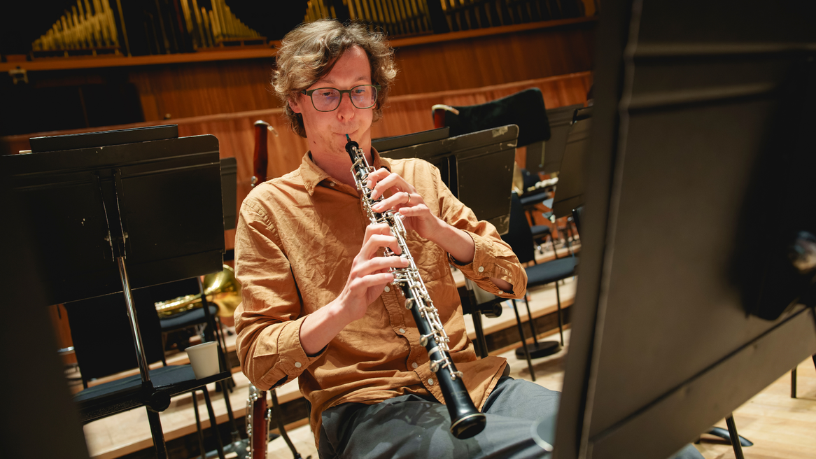 A man sits on a chair playing the oboe