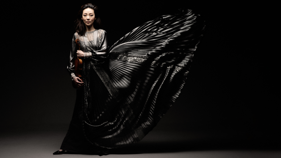 A woman in a dramatic flowing black dress holds a violin