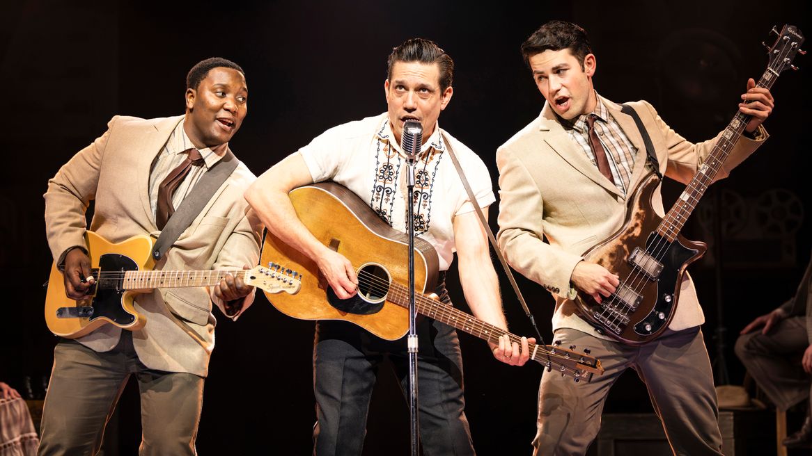 Three men play guitars while one sings into an old fashioned microphone