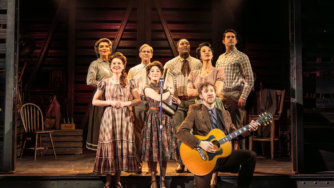 Four women and four men smile, one man holds a guitar and a woman holds an old fashioned instrument