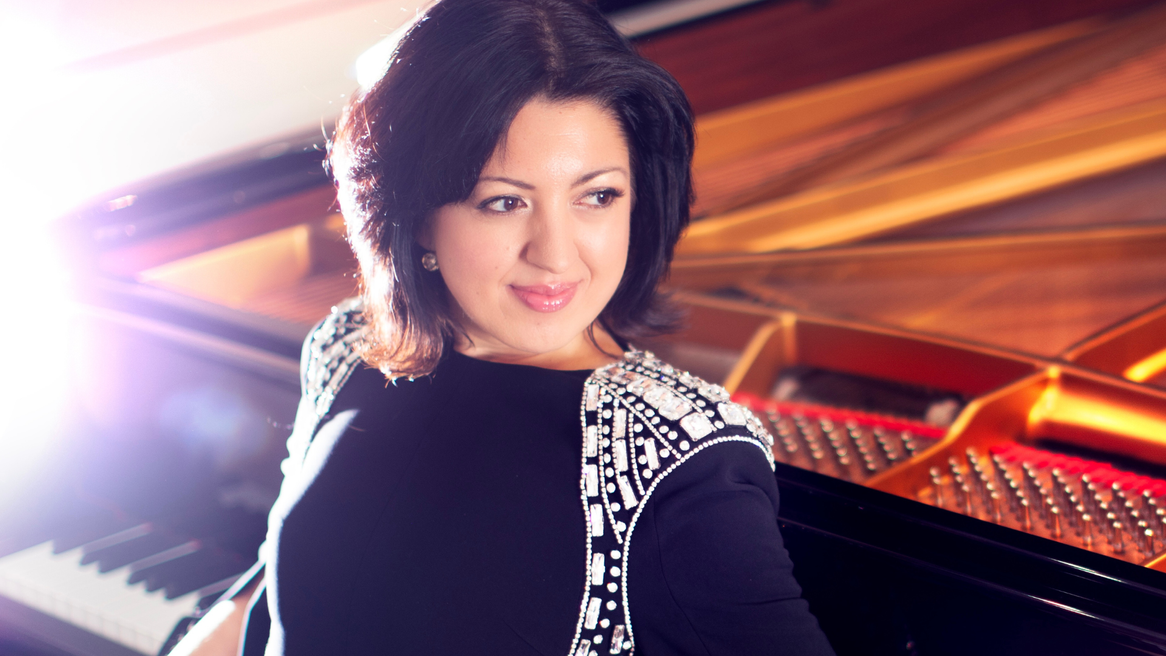 A woman in a black and white dress leans against a piano
