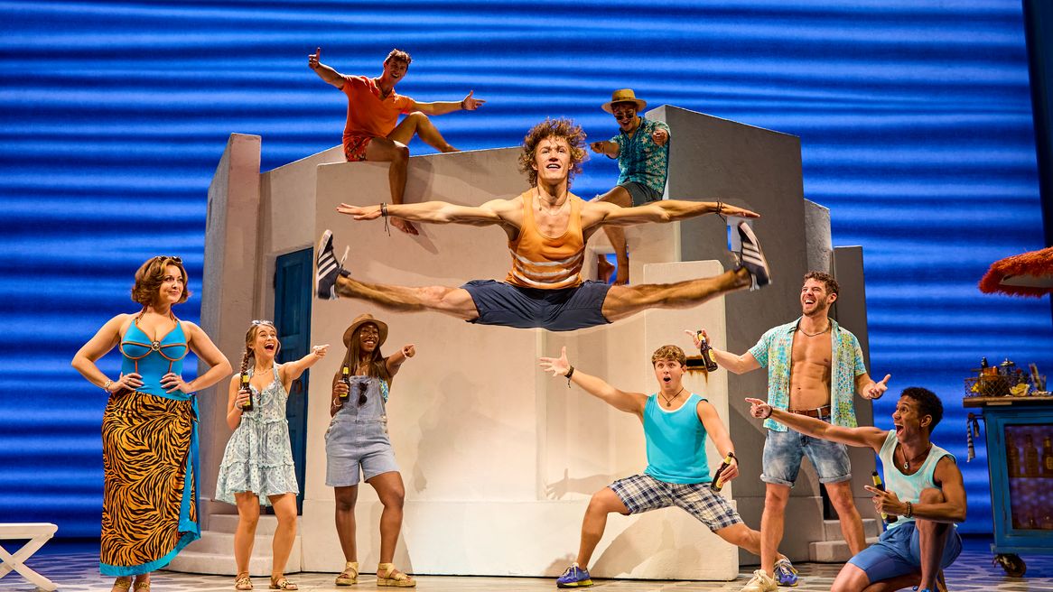 A young man does the splits in the air as people cheer on