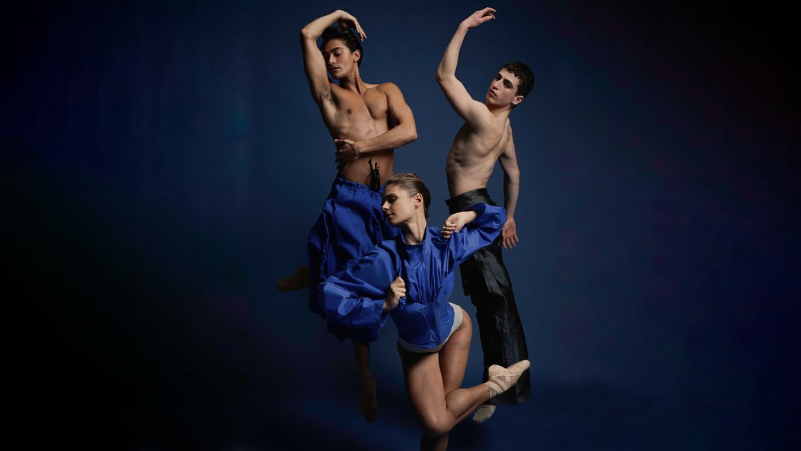 Three ballet dancers pose in front of a blue background