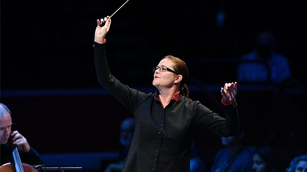 A woman with glasses raises a conductor's baton