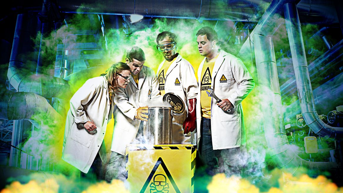Four peple dressed as scientists surrounded by yellow smoke pour liquid into a toxic can