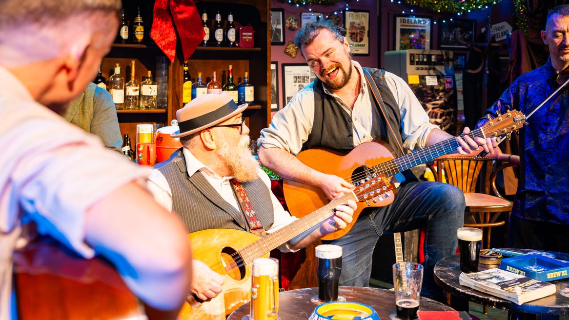 A man sings as he plays guitar with an older bearded man