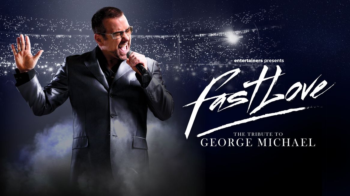 A man dressed in a black suit and glasses in the style of George Michael sings into a microphone in front of a large audience