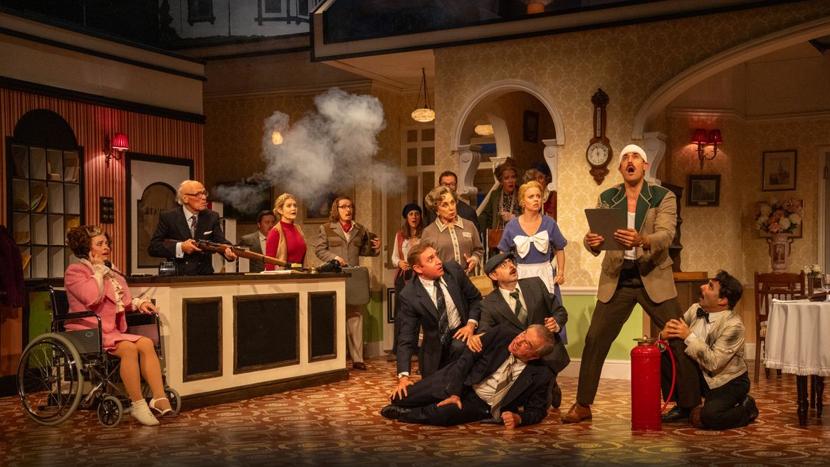 A group of people stand in a hote lreception looking shcoekd while one man holds a smoking gun