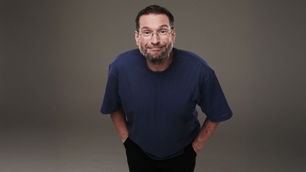 Comedian Gary Delaney in a blue t-shirt grinning at the camera 