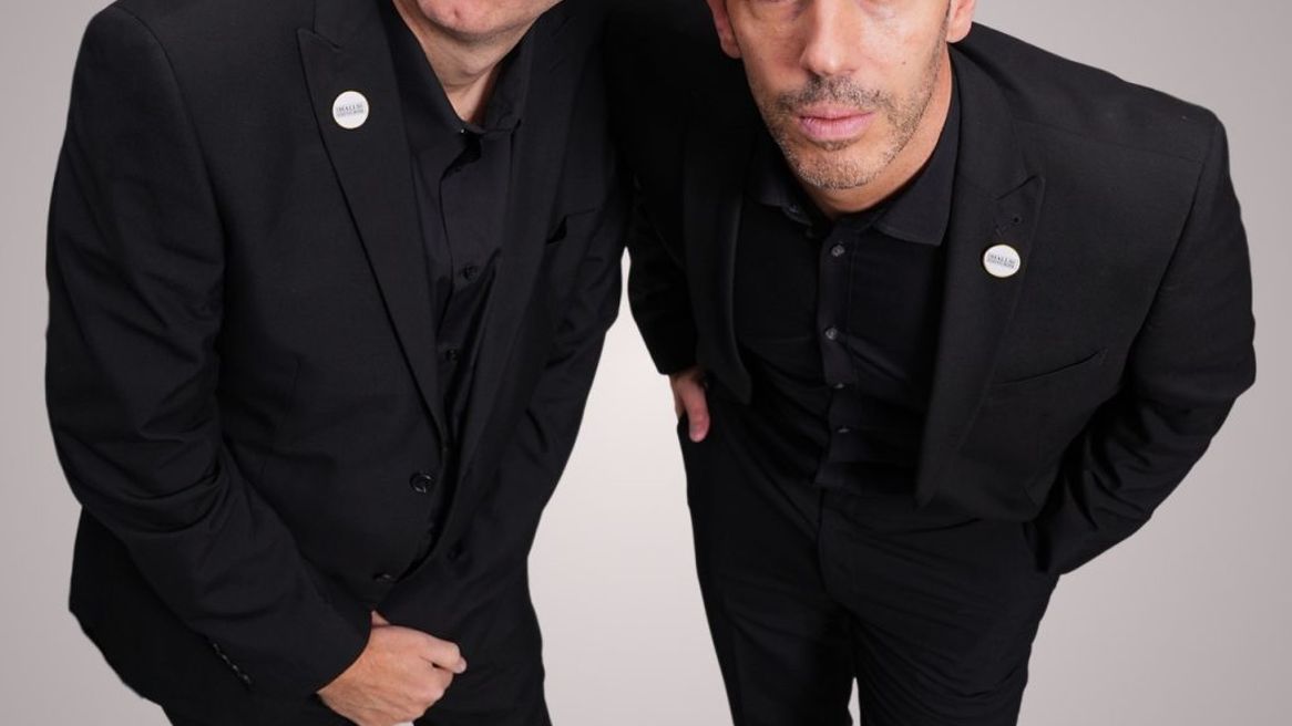 Two comedians in black suits looking up towards the camera