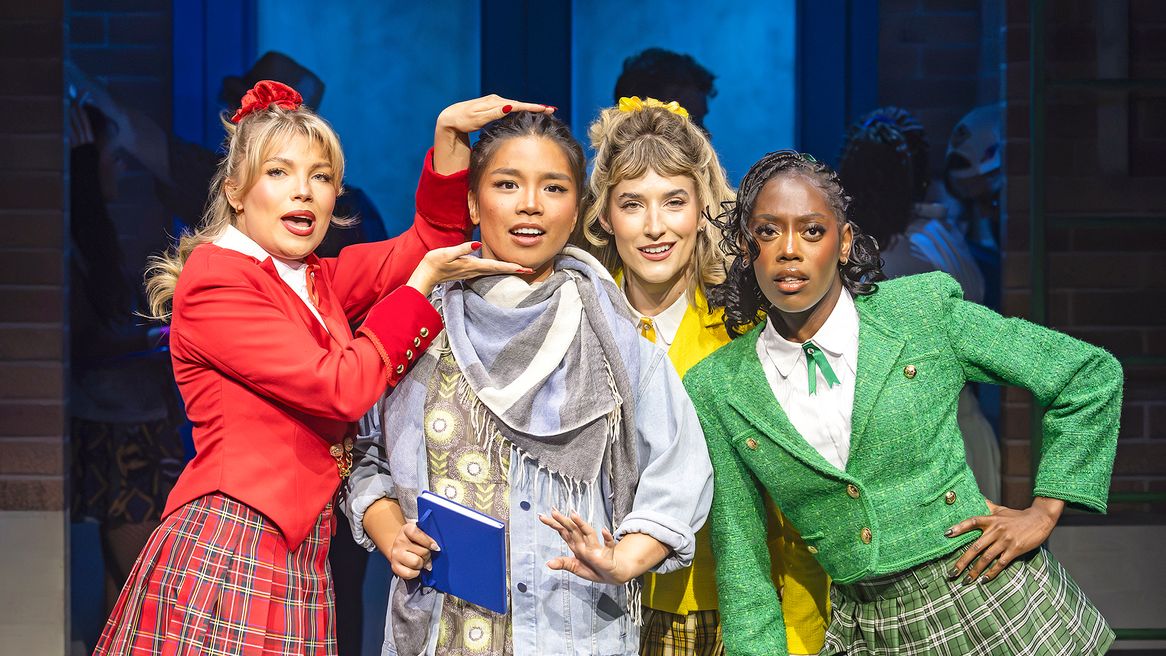 Three girls in matching red, yellow and green outfits frame the face of a girl in ugly clothing.