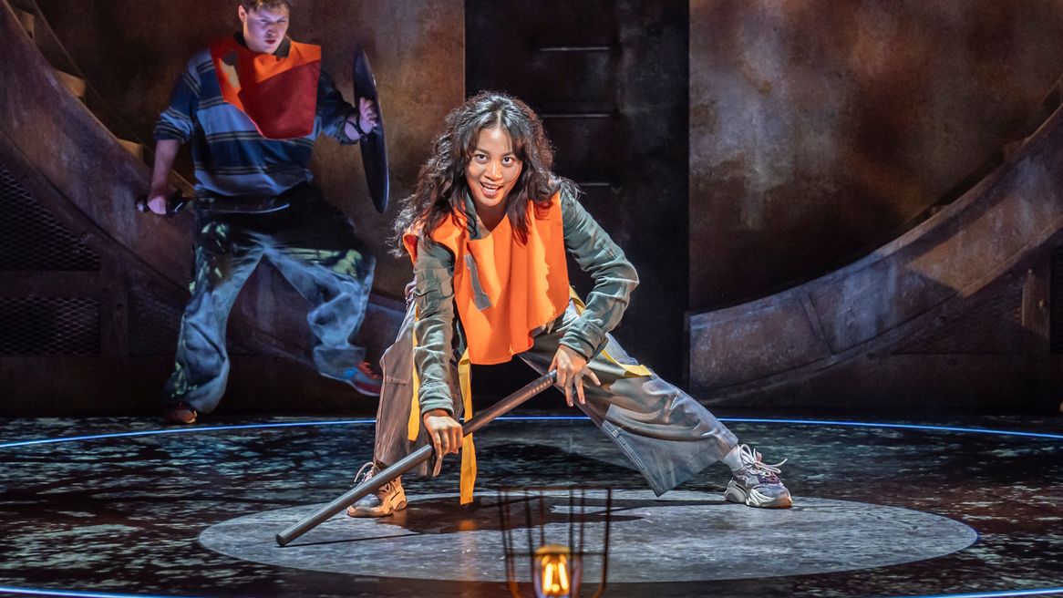 A fierce looking girl kneels down holding a pole on the floor 