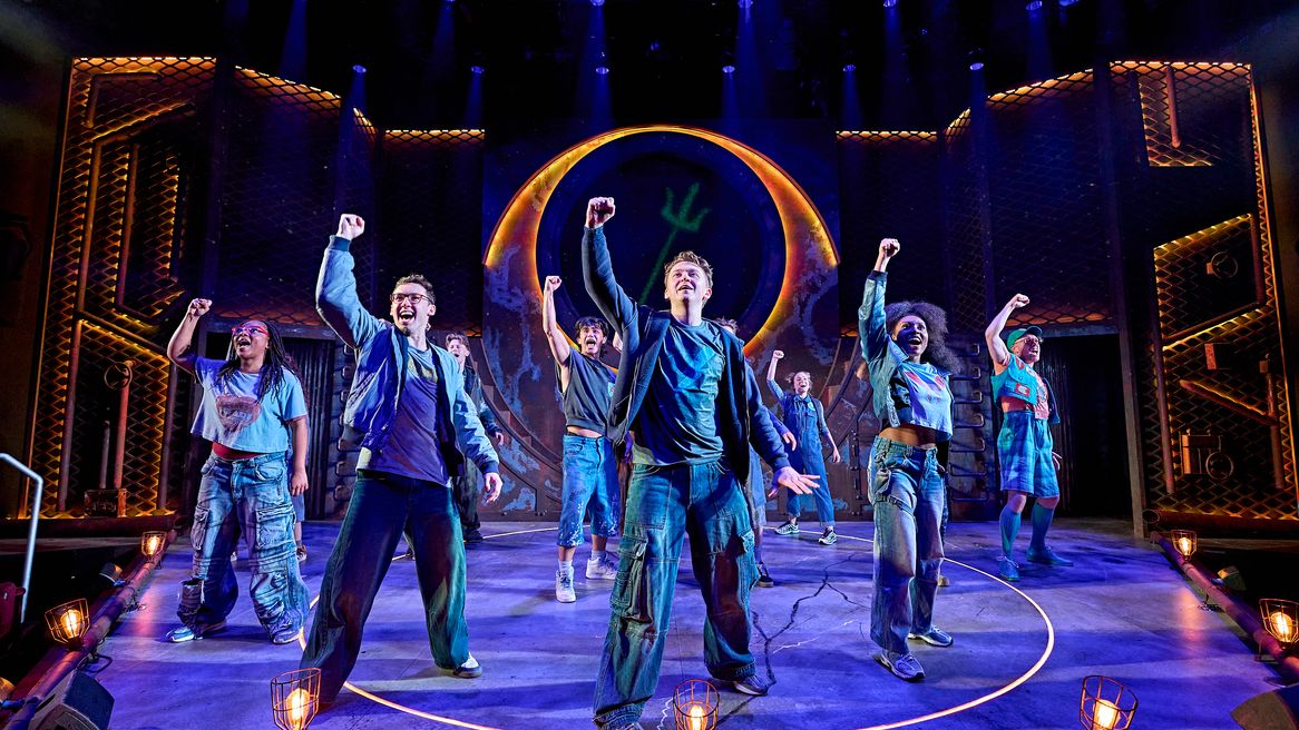 A group of young people stand with their fists raised in front of an image of the Trident of Poseidon