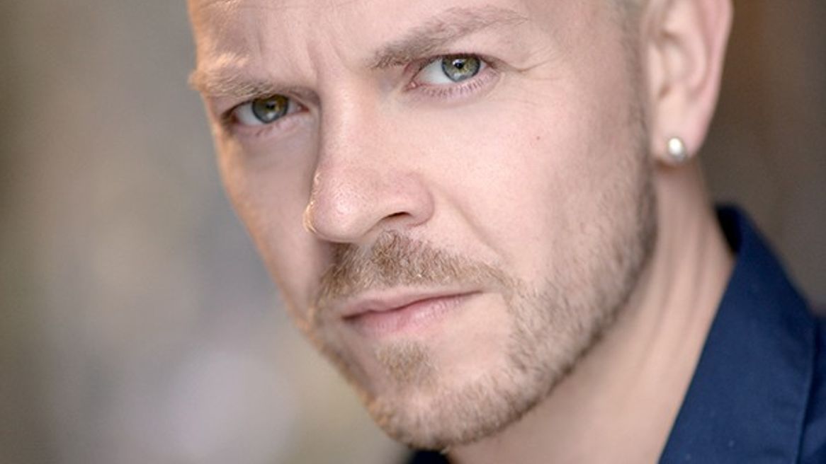 Man with blond cropped hair stares at the camera