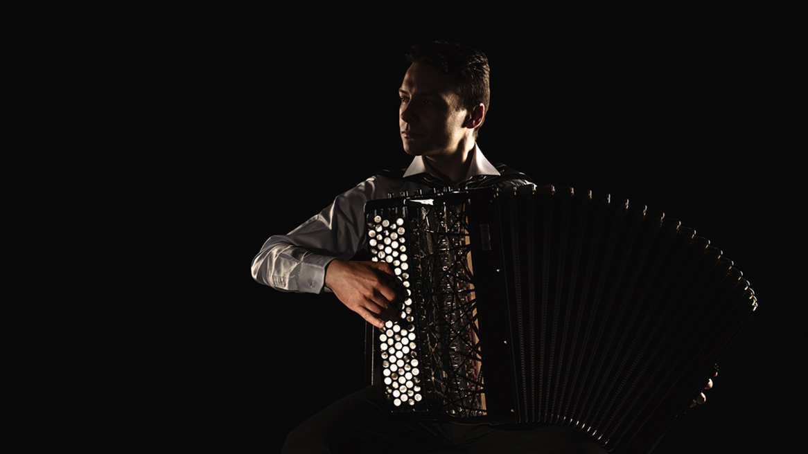 A man stands in the shadows holding an accordion