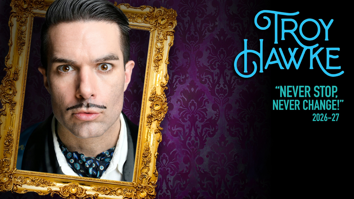 A dark haired, moustached man in a blue satin jacket and cravat pouts with his head through an ornate gold frame