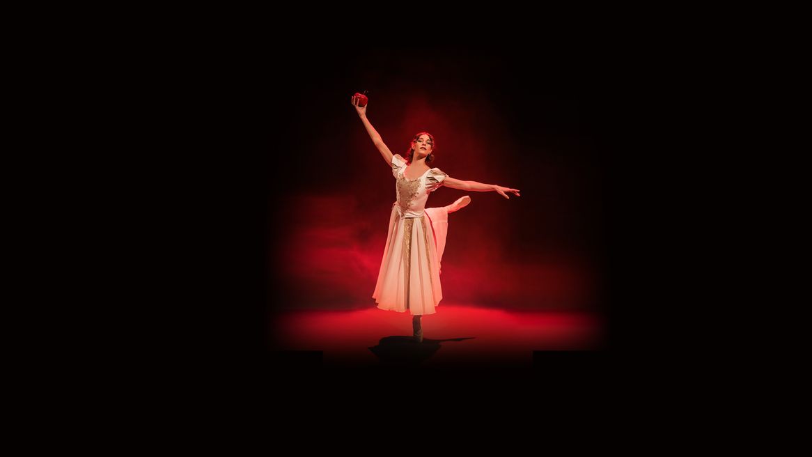 A young ballet dancer stands en pointe with an apple in her hand