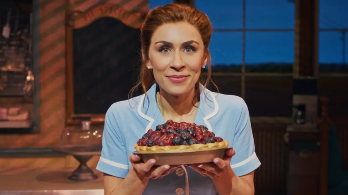 A young woman in a blue waitress uniform holds a berry pie